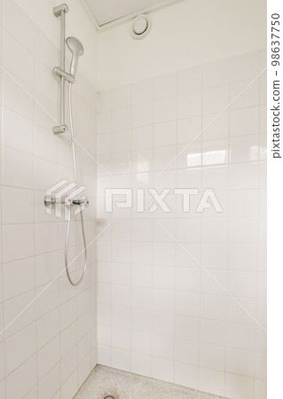 a bathroom with white tiles on the walls and floor, including a shower head mounted in the corner of the bathtub 98637750