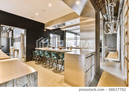 Contemporary minimalist style interior design of light studio apartment with wooden table and chairs in dining zone between open kitchen and living room with white walls and parquet floor 98637792