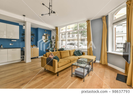 a living room with blue walls and wood flooring the room has a yellow couch, coffee table, two chairs, and a 98637793