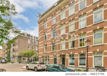 some cars parked on the side of a street in front of a large brick building with many windows and doors 98637794