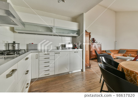 a kitchen and dining area in a house with white cabinets, wood flooring and an open door leading to the living room 98637820