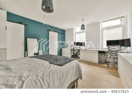 a bedroom with a bed, desk and computer monitor on the wall in front of the bed is dark teal blue a bedroom with a bed, desk and computer monitor on the wall in front of the bed is dark teal blue 98637823