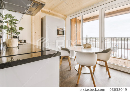 Home interior design of modern loft apartment with open kitchen in minimalist style and spacious dining zone with table and chairs 98638049