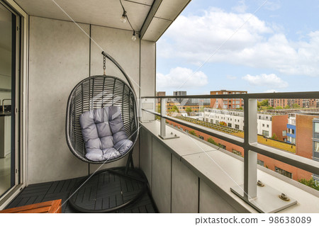 a balcony with a hanging chair on the left and a view of buildings in the back ground to the right 98638089