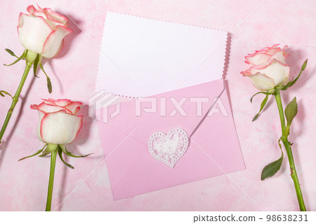 Pink envelope with empty white blank sheet and pale pink roses on pink backdrop. Copy space Top view Pink envelope with empty white blank sheet and pale pink roses on pink backdrop. Copy space Top view 98638231