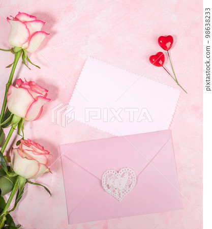 Festive flat lay arrangement of pale pink roses, envelope, hearts, empty white blank sheet on pink. Festive flat lay arrangement of pale pink roses, envelope, hearts, empty white blank sheet on pink. 98638233