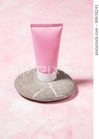 Pink blank cosmetic tube standing on natural rounded smooth boulder on pink background. Copy space. Pink blank cosmetic tube standing on natural rounded smooth boulder on pink background. Copy space. 98638241