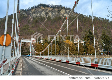 a suspension bridge over a river in the mountains. A road for cars and part for pedestrians 98639973