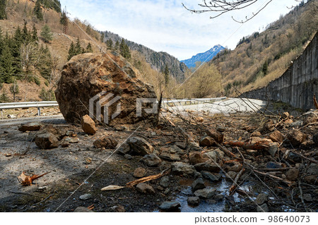 A huge rock fell from the mountains onto the road, destroying the asphalt and blocking half of the roadway A huge rock fell from the mountains onto the road, destroying the asphalt and blocking half of the roadway 98640073