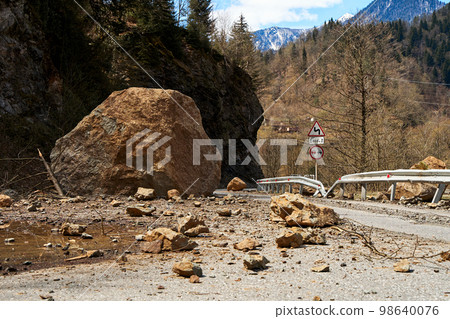 A huge rock fell from the mountains onto the road, destroying the asphalt and blocking half of the roadway 98640076