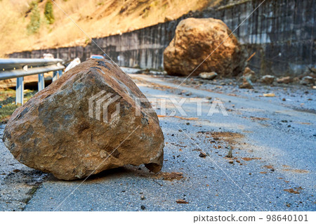 A huge rock fell from the mountains onto the road, destroying the asphalt and blocking half of the roadway A huge rock fell from the mountains onto the road, destroying the asphalt and blocking half of the roadway 98640101