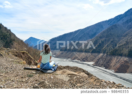 A girl on a picnic with an incredible natural view of the mountains and a dehydrated mountain river. Gorgeous scenery 98640355