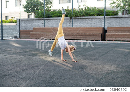 Caucasian girl makes a cartwheel on the sports field outdoors.  98640892