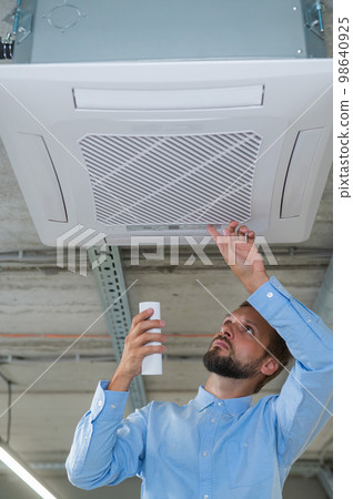 Caucasian bearded man repairing the air conditioner in the office. Caucasian bearded man repairing the air conditioner in the office. 98640925