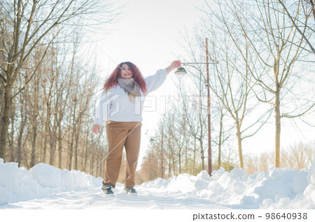 Smiling plump redhead woman jumping in park in winter.  98640938