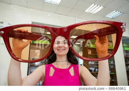 Caucasian woman holding huge red decorative glasses. Caucasian woman holding huge red decorative glasses. 98640961