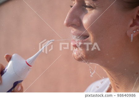 A woman with braces on her teeth uses an irrigator. Close-up portrait. A woman with braces on her teeth uses an irrigator. Close-up portrait. 98640986