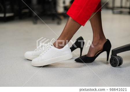 African woman changing from high heels to sneakers in the office. Tired legs.  98641021