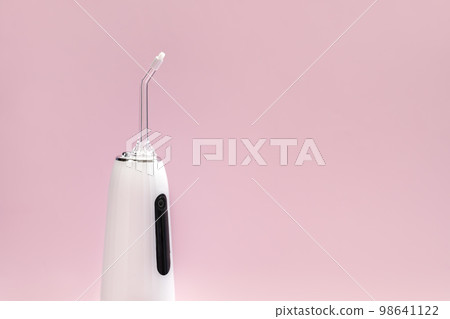 Cropped Oral teeth irrigator, dental water tooth cleaner, white portable rechargeable cordless water dental flosser on pink background. Waterproof home dental care device with nozzle. Horizontal 98641122