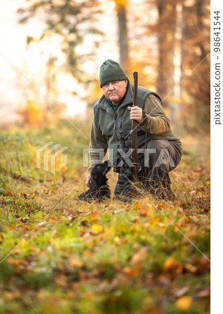 Hunter or ranger with a professional, nightvision hunting gun and hunting form to hunt in an autumn forest, hunting concept Hunter or ranger with a professional, nightvision hunting gun and hunting form to hunt in an autumn forest, hunting concept 98641544