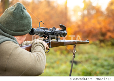 Hunter or ranger with a professional, nightvision hunting gun aiming wild animal and hunting form to hunt in an autumn forest, hunting concept Hunter or ranger with a professional, nightvision hunting gun aiming wild animal and hunting form to hunt in an autumn forest, hunting concept 98641548