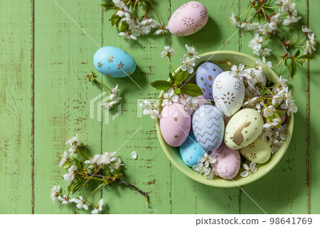 Easter composition. Branches of a blooming apple tree, handmade Easter colorful eggs on a pastel rustic wooden table. Happy Easter Holidays. View from above. 98641769