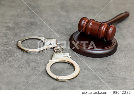 Law theme. Court of law trial in session. Judge gavel handcuffs on grey table in lawyer office or court session. Mallet of judge on concrete stone grey background. Justice human rights concept Law theme. Court of law trial in session. Judge gavel handcuffs on grey table in lawyer office or court session. Mallet of judge on concrete stone grey background. Justice human rights concept 98642282