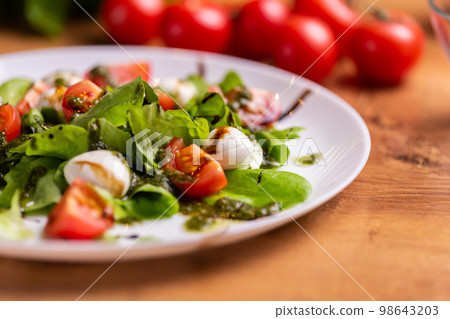 Plate of healthy classic close-up caprese salad with mozzarella cheese tomatoes and basil in kitchen - italian cuisine Plate of healthy classic close-up caprese salad with mozzarella cheese tomatoes and basil in kitchen - italian cuisine 98643203