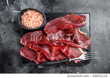 Turkish sliced pastrami (kayseri pastirma), dried beef meat with spices on marble board. Black background. Top view 98643218
