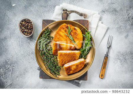 Chicken fried Cordon bleu cutlet with ham and cheese on a plate with herbs. White background. Top view 98643232