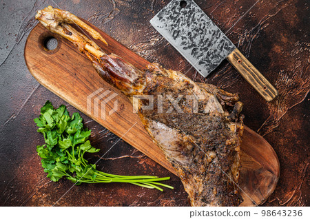Roast lamb leg meat with herbs and spices on a cutting board. Dark background. Top view 98643236