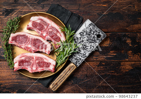 Uncooked Raw lamb loin chops steaks, saddle in plate with rosemary and thyme. Wooden background. Top view. Copy space 98643237