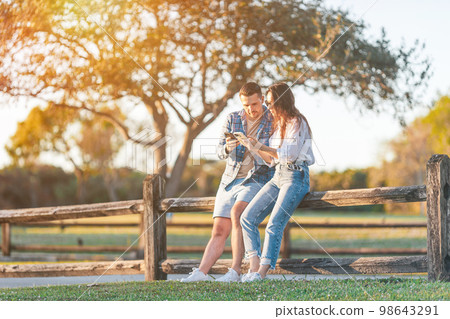 Family of two in the park on summer day using smartphone 98643291