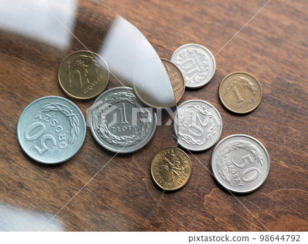 Poland's currency, zloty and groszy, under magnifying glass on the wooden table, selective focus. Local European currencies 98644792