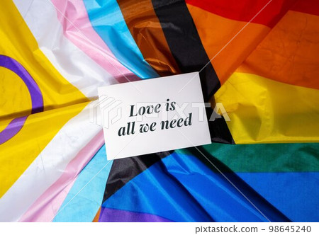 LOVE IS ALL WE NEED text on valentine card inscription positive quote phrase Greeting card on Rainbow LGBTQIA flag made from silk material. Symbol of LGBTQ pride month. Equal rights. Peace and freedom 98645240
