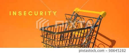 INSECURITY text Empty shopping trolley cart on colorful orange background. Online shopping, buy mall market shop consumer concept. Small toy supermarket grocery push cart. Rising food cost, grocery 98645282