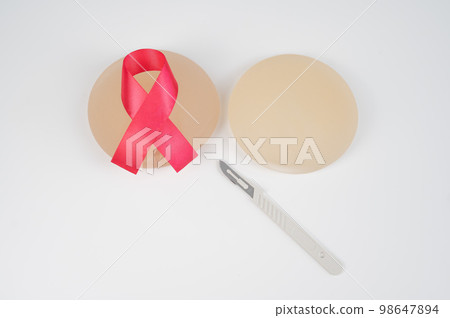 Breast silicone implants, pink tape and a disposable scalpel on a white background. Breast silicone implants, pink tape and a disposable scalpel on a white background. 98647894