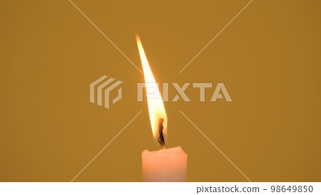 A single wax candle burning on a yellow background A single wax candle burning on a yellow background 98649850