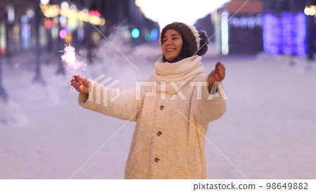 Portrait of young smiling Caucasian woman holding sparklers. Happy cheerful girl outdoors Celebrating New Year holidays vacation. Xmas Christmas winter atmosphere. 3840x2160 Portrait of young smiling Caucasian woman holding sparklers. Happy cheerful girl outdoors Celebrating New Year holidays vacation. Xmas Christmas winter atmosphere. 3840x2160 98649882