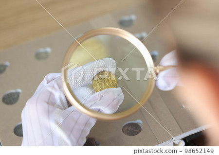 Numismatist in gloves looks through magnifying glass and evaluates ancient coins. Numismatist in gloves looks through magnifying glass and evaluates ancient coins. 98652149