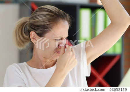 Upset middle age woman stands and smells her armpit. Upset middle age woman stands and smells her armpit. 98652159