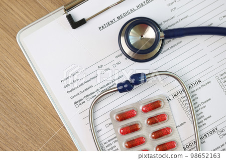 Blank sheet of patient's medical history form with stethoscope and pills, top view. 98652163
