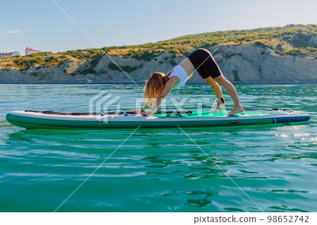 Young woman make yoga or gymnastic on stand up paddle board in quiet sea Young woman make yoga or gymnastic on stand up paddle board in quiet sea 98652742