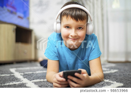 A child boy with phone and headphones is lying on the floor A child boy with phone and headphones is lying on the floor 98653966
