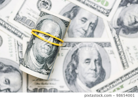 A roll of 100 dollar bills close-up on a pile of American dollars 98654001