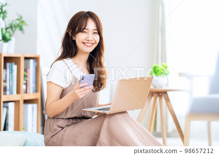 一位女士在客廳操作電腦和智能手機 98657212