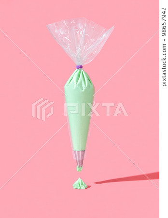 Frosting bag isolated on a pink background. Green buttercream icing in a plastic bag Frosting bag isolated on a pink background. Green buttercream icing in a plastic bag 98657942