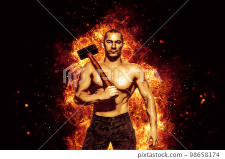 Strong man with naked torso holds a sledgehammer while isolated on burning background. Copy Space  98658174