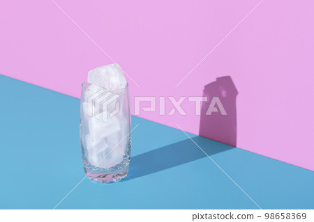 Ice cubes in a glass, in bright light, minimalist on a blue and pink background 98658369