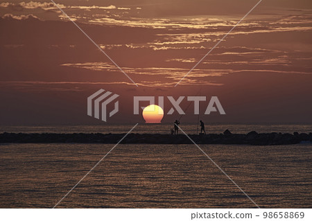 The sun appears among the fishermen on the breakwater 98658869